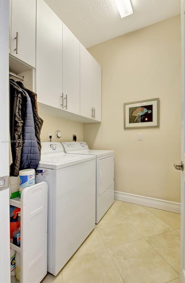 washroom with washer and dryer, light tile patterned flooring, cabinets, and a textured ceiling