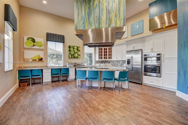 kitchen featuring a breakfast bar, backsplash, light hardwood / wood-style floors, white cabinetry, and stainless steel appliances