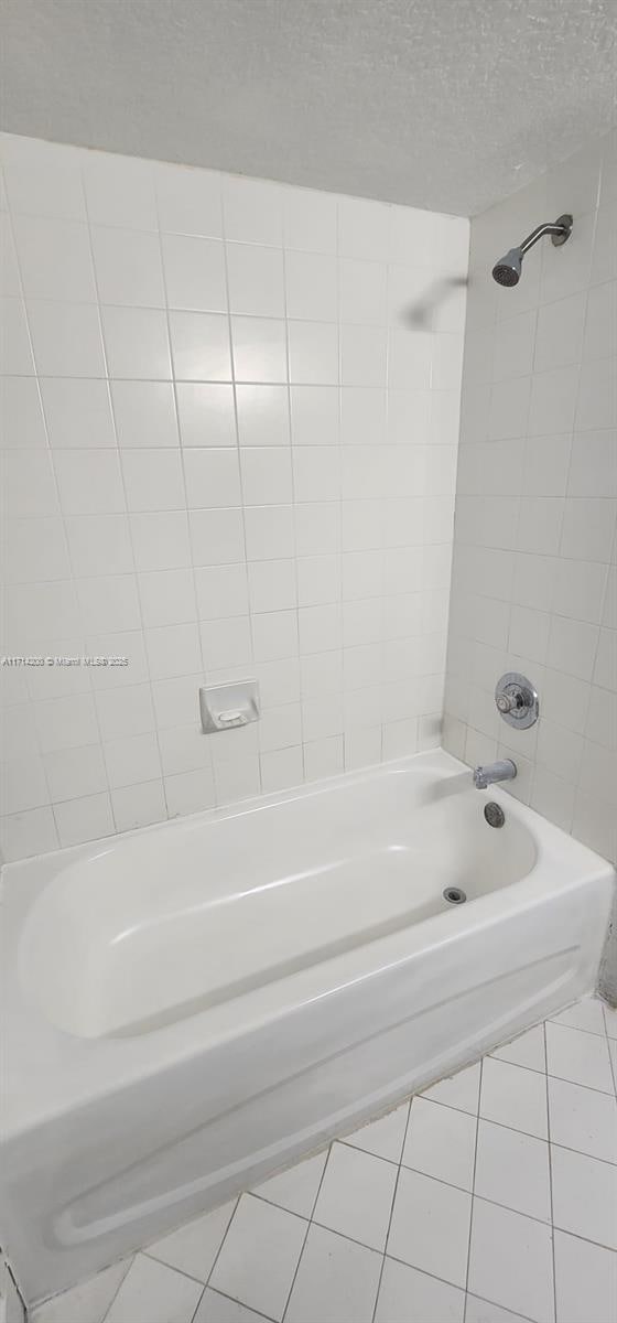 bathroom with tile patterned flooring, tiled shower / bath, and a textured ceiling