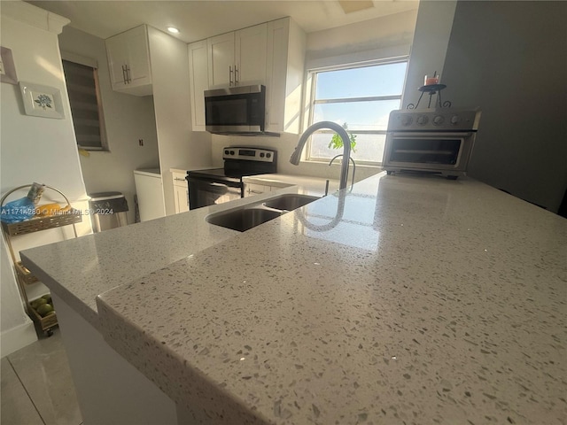 kitchen with kitchen peninsula, appliances with stainless steel finishes, light stone counters, sink, and white cabinets