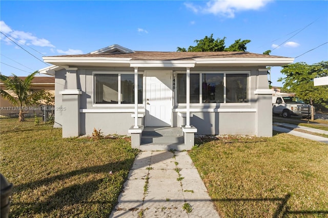 bungalow-style home with fence, a front lawn, and stucco siding