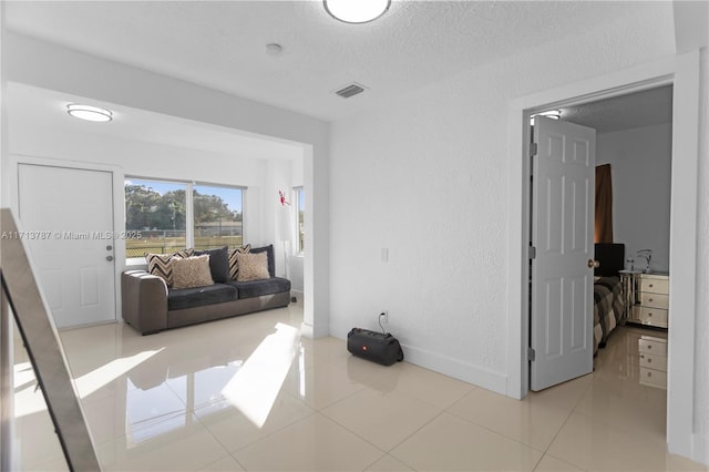 interior space featuring baseboards, visible vents, a textured wall, tile patterned flooring, and a textured ceiling