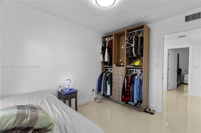 bedroom with tile patterned flooring, a closet, visible vents, and a textured ceiling