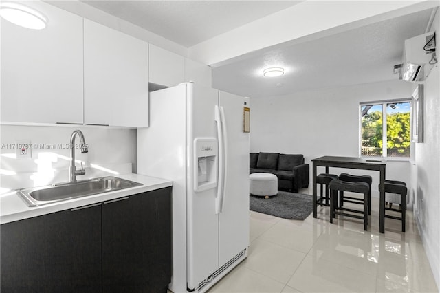 kitchen with light tile patterned floors, light countertops, white cabinets, a sink, and white fridge with ice dispenser