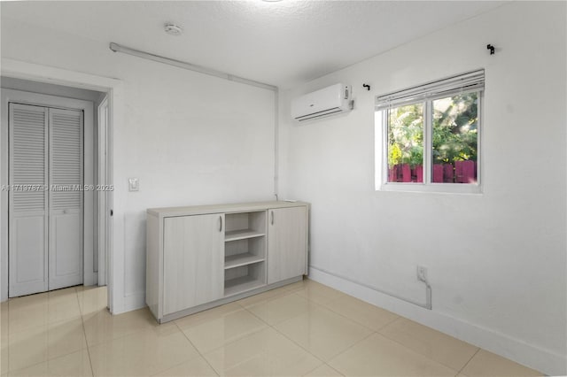 unfurnished bedroom with light tile patterned floors, a textured ceiling, a wall unit AC, and baseboards