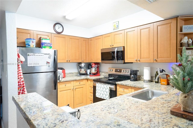 kitchen with kitchen peninsula, appliances with stainless steel finishes, light stone counters, and sink