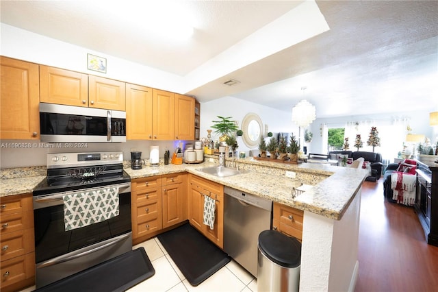 kitchen with kitchen peninsula, stainless steel appliances, a notable chandelier, and sink