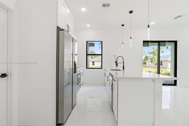 kitchen featuring stainless steel fridge, a kitchen island with sink, sink, pendant lighting, and white cabinets