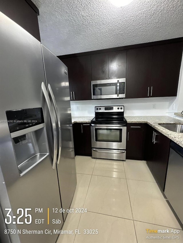 kitchen featuring appliances with stainless steel finishes, light stone counters, dark brown cabinets, sink, and light tile patterned floors