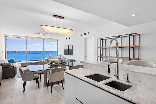 kitchen featuring light stone countertops, pendant lighting, a water view, and sink