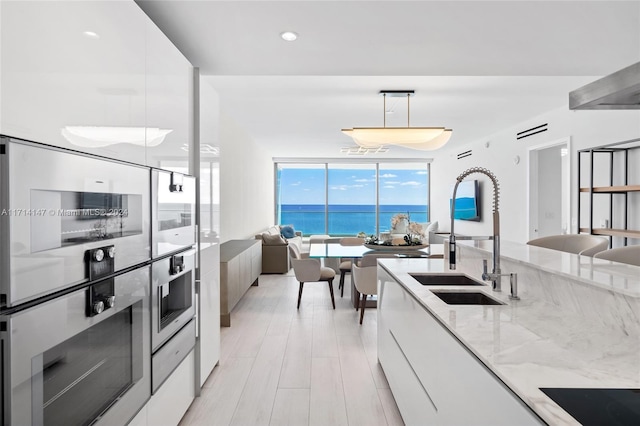 kitchen featuring white cabinetry, sink, a water view, and pendant lighting