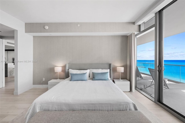 bedroom featuring access to exterior, a water view, light hardwood / wood-style flooring, a wall of windows, and a beach view