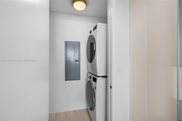 laundry area featuring light wood-type flooring, stacked washing maching and dryer, and electric panel