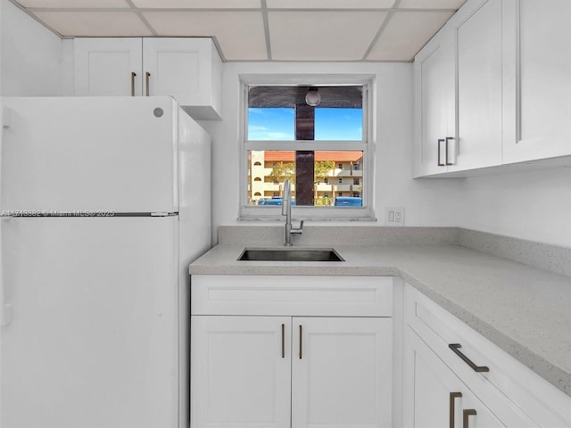 kitchen featuring white cabinetry, sink, white fridge, light stone countertops, and a drop ceiling