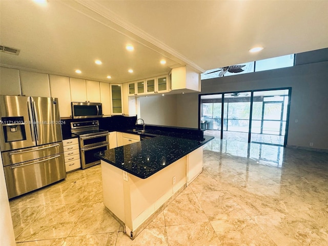 kitchen with a breakfast bar, kitchen peninsula, dark stone countertops, appliances with stainless steel finishes, and white cabinetry