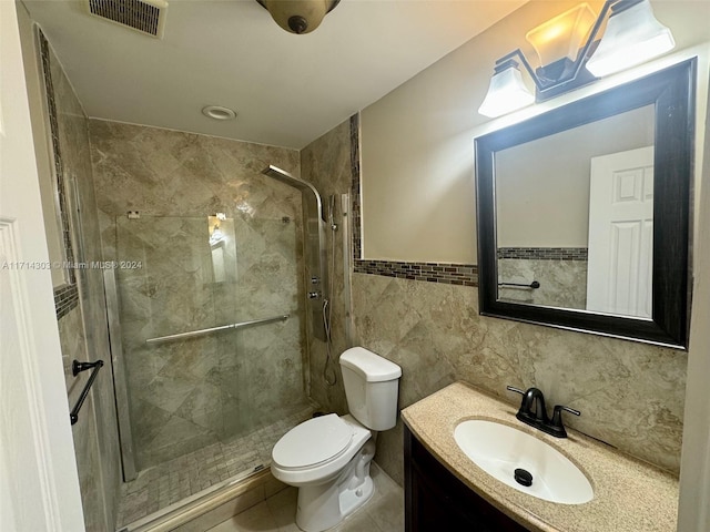 bathroom with a tile shower, tile patterned flooring, toilet, vanity, and tile walls