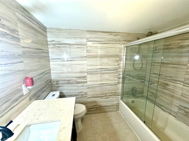 full bathroom with tile patterned flooring, toilet, shower / bath combination with glass door, vanity, and tile walls