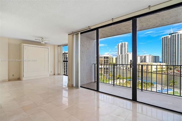 unfurnished room featuring ceiling fan, a water view, a textured ceiling, and a wall of windows