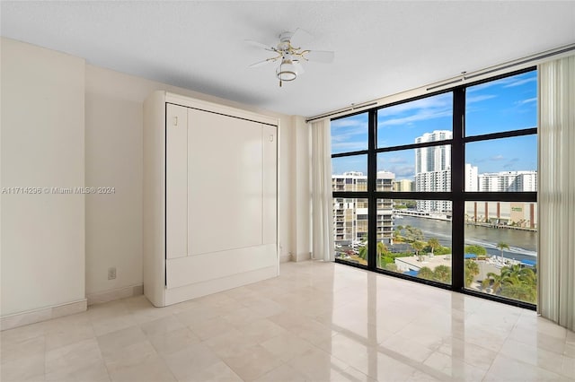 unfurnished room featuring floor to ceiling windows, ceiling fan, a water view, and a healthy amount of sunlight