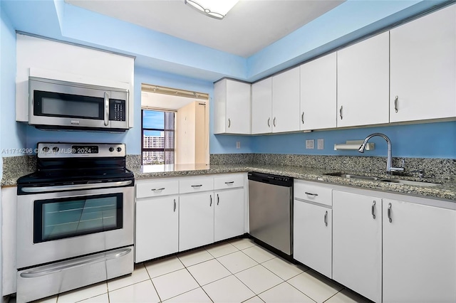 kitchen featuring appliances with stainless steel finishes, dark stone counters, sink, white cabinets, and light tile patterned flooring