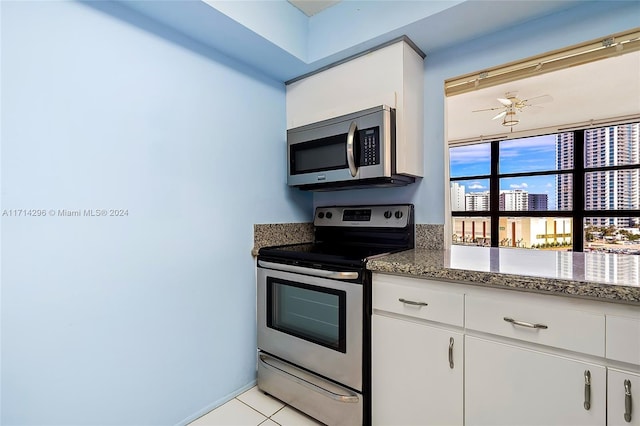 kitchen featuring stainless steel appliances, ceiling fan, dark stone countertops, white cabinetry, and light tile patterned flooring