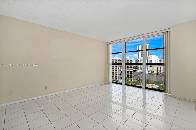 empty room with a water view, floor to ceiling windows, and light tile patterned floors