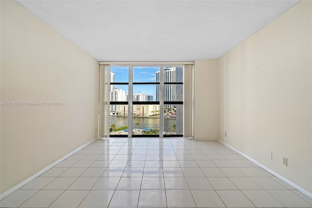 unfurnished room featuring floor to ceiling windows, a water view, and light tile patterned flooring