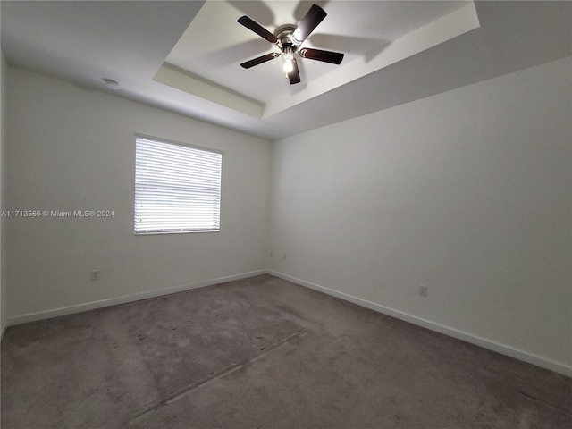 empty room with a tray ceiling, ceiling fan, and dark colored carpet