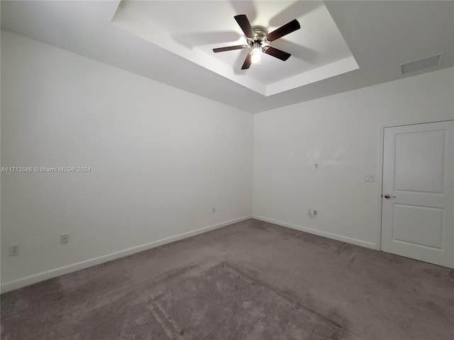 empty room with a tray ceiling, ceiling fan, and carpet