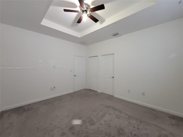 carpeted empty room with a raised ceiling and ceiling fan