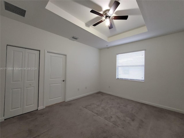 unfurnished bedroom with a raised ceiling, ceiling fan, a closet, and light colored carpet