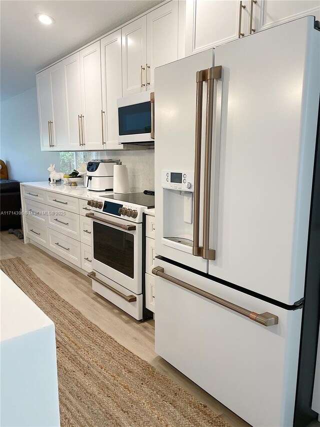 kitchen featuring white appliances, a center island with sink, white cabinets, vaulted ceiling, and decorative light fixtures