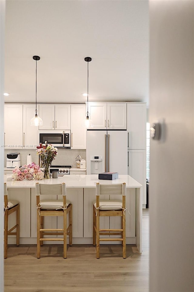 kitchen with stainless steel microwave, light wood-style flooring, a kitchen breakfast bar, white refrigerator with ice dispenser, and white cabinetry