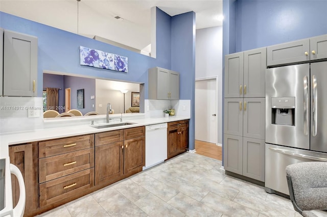 kitchen featuring stainless steel refrigerator with ice dispenser, white dishwasher, sink, a high ceiling, and gray cabinets