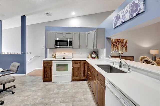 kitchen with gray cabinetry, sink, vaulted ceiling, white appliances, and light tile patterned flooring