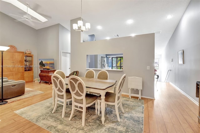 dining space featuring high vaulted ceiling, ceiling fan with notable chandelier, and light wood-type flooring