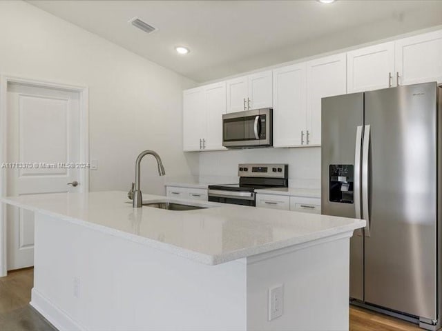 kitchen with appliances with stainless steel finishes, an island with sink, white cabinets, light hardwood / wood-style flooring, and sink