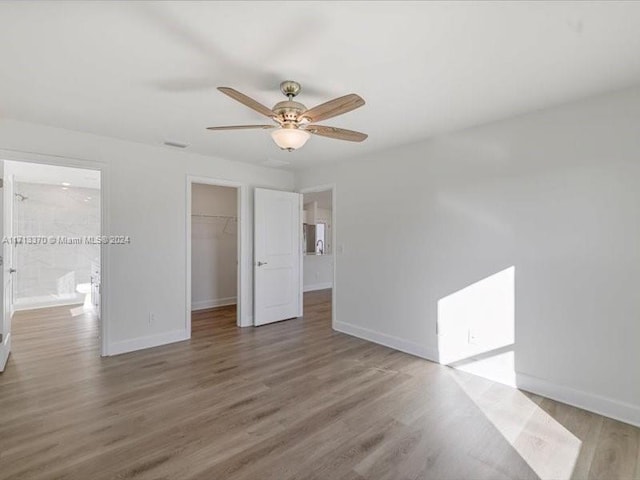 unfurnished bedroom with a spacious closet, hardwood / wood-style floors, ceiling fan, a closet, and ensuite bath