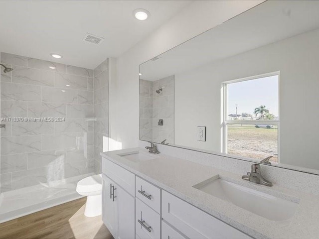 bathroom with toilet, wood-type flooring, vanity, and tiled shower