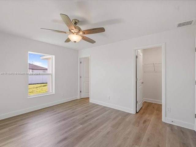 unfurnished bedroom featuring a closet, ceiling fan, light hardwood / wood-style floors, and a spacious closet