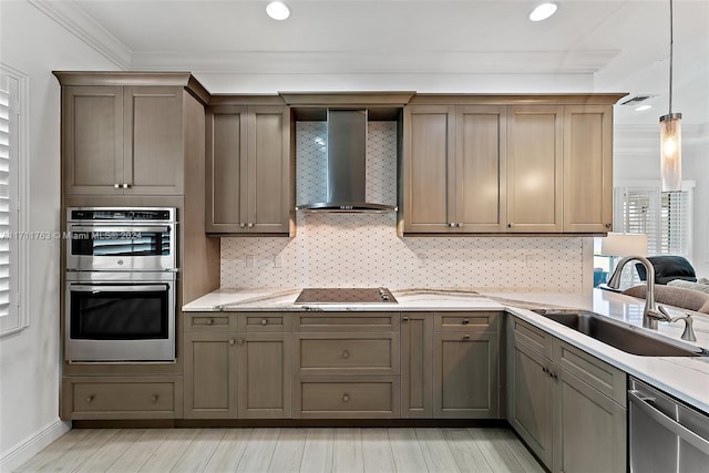 kitchen with wall chimney range hood, sink, ornamental molding, decorative light fixtures, and stainless steel appliances