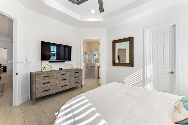 bedroom featuring a raised ceiling, ensuite bathroom, and ceiling fan