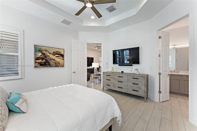 bedroom featuring a raised ceiling, connected bathroom, and ceiling fan