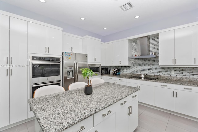 kitchen with wall chimney exhaust hood, stainless steel appliances, light tile patterned flooring, backsplash, and white cabinets