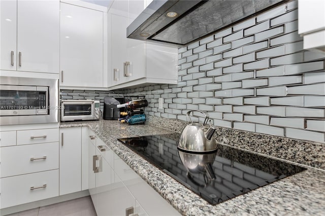 kitchen featuring white cabinets, stainless steel microwave, light tile patterned floors, and light stone counters