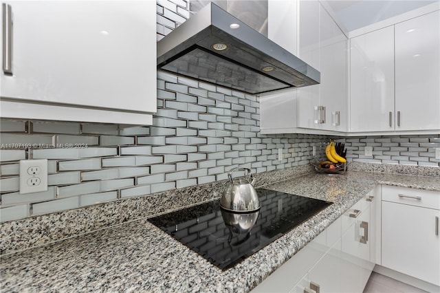 kitchen with white cabinetry, light stone counters, wall chimney range hood, and black electric cooktop