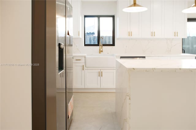 kitchen featuring light stone countertops, sink, white cabinets, and pendant lighting