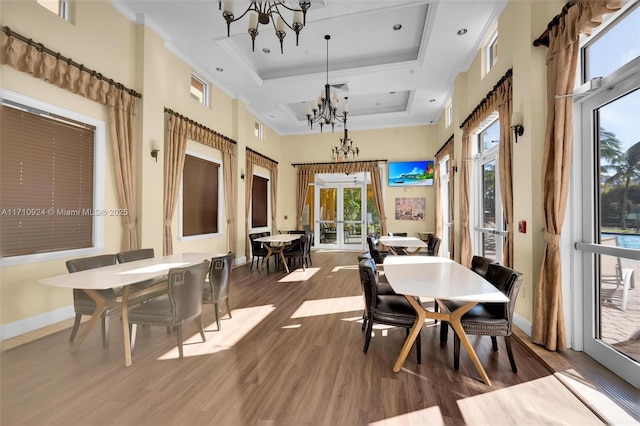 dining space with a notable chandelier, hardwood / wood-style floors, a high ceiling, a raised ceiling, and ornamental molding