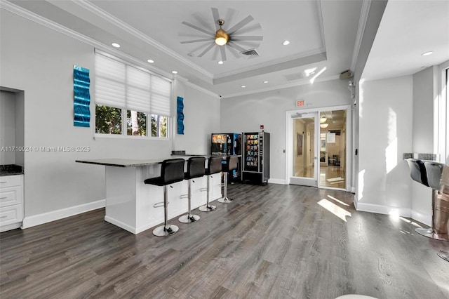 kitchen with white cabinets, dark wood-type flooring, ornamental molding, a raised ceiling, and a breakfast bar