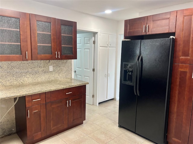 kitchen featuring backsplash, light stone countertops, black fridge with ice dispenser, and light tile patterned floors